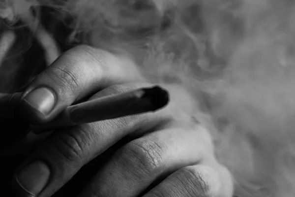 Καπνού σε μαύρο φόντο. Ένας άνθρωπος καπνίζει κάνναβη ζιζανίων, ένα κοινό και ένα ελαφρύτερο στα χέρια του. Έννοιες της ιατρική χρήση μαριχουάνα και τη νομιμοποίηση της κάνναβης. Σε μαύρο φόντο μαύρο και άσπρο — Φωτογραφία Αρχείου