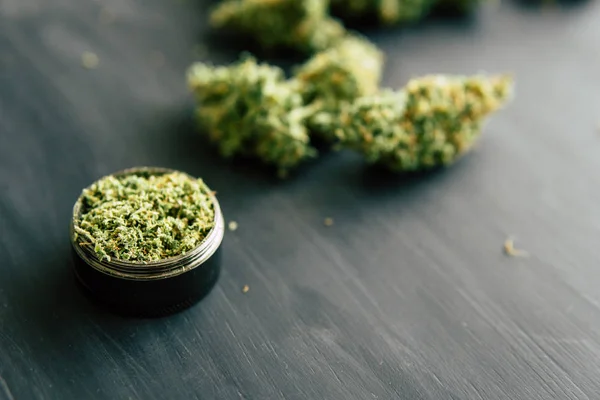 Macro di marijuana con tricomi e erba tritata in un tritacarne per tagliare una canapis su un tavolo nero — Foto Stock