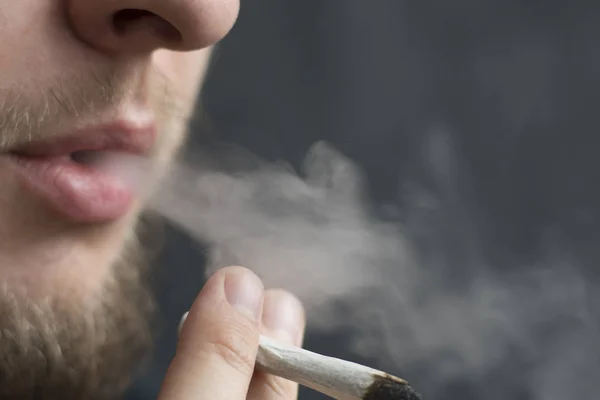 Un hombre fuma marihuana, un porro y un encendedor en sus manos. Humo sobre fondo negro. Conceptos de uso médico de la marihuana y legalización del cannabis . — Foto de Stock