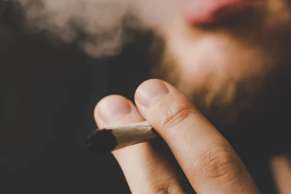 Humo sobre fondo negro. Un hombre fuma marihuana, un porro y un encendedor en sus manos. Conceptos de uso médico de la marihuana y legalización del cannabis . —  Fotos de Stock
