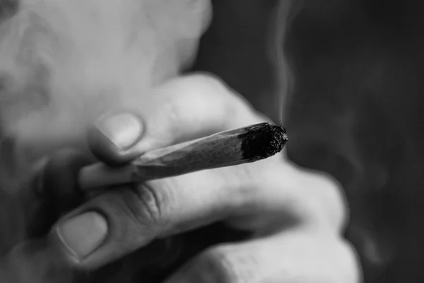 Roken op een zwarte achtergrond. Een man rookt cannabis onkruid, een gezamenlijke en een aansteker in zijn handen. Begrippen medisch marihuanagebruik en legalisatie van de cannabis. Zwart-wit — Stockfoto