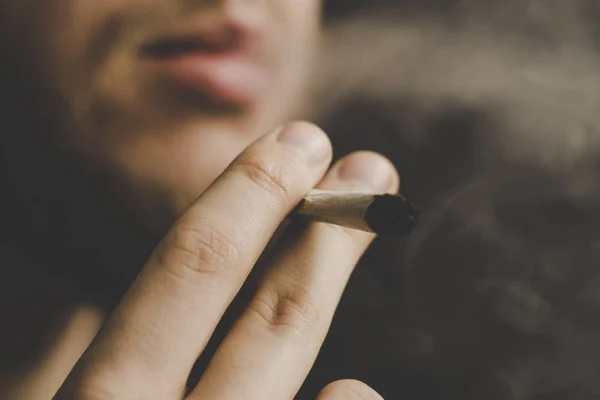 Κάνναβης ζιζανίων Α άνθρωπος καπνίζει, μια κοινή και ένα ελαφρύτερο στα χέρια του. Καπνού σε μαύρο φόντο. Έννοιες της ιατρική χρήση μαριχουάνα και τη νομιμοποίηση της κάνναβης. — Φωτογραφία Αρχείου