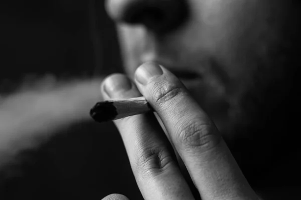 Kannabisz gyom A férfi dohányzik, egy közös és egy könnyebb a kezében. A füst a fekete háttér. Fogalmak és a kannabisz legalizálása orvosi marihuána. Fekete-fehér — Stock Fotó