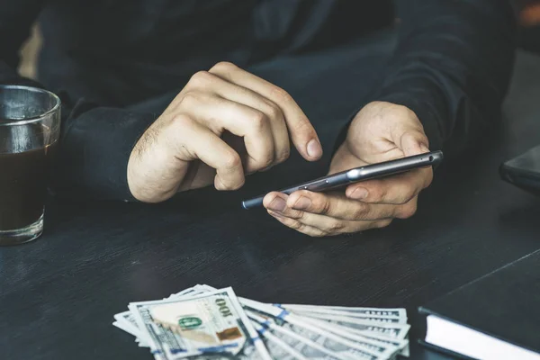 Technology, online banking, money transfer, e-commerce concept. Businessman using smartphone dollar bills flying on grey wall background. Internet earnings concept