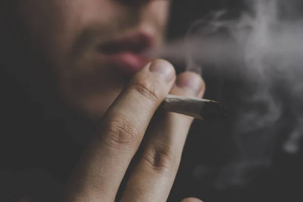 一个男人在手上抽大麻,。黑色背景下的烟雾。医用大麻的概念与大麻合法化. — 图库照片