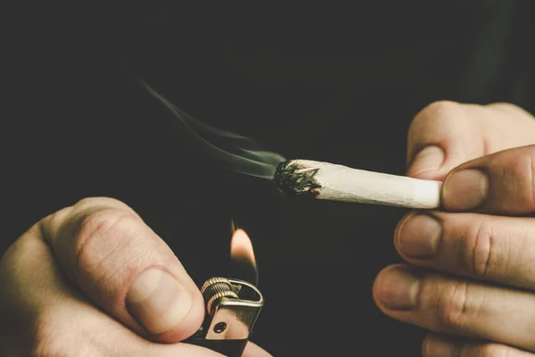 Articulación en mano. Un hombre fuma marihuana, una. Humo sobre fondo negro. Conceptos de uso médico de la marihuana y legalización del cannabis . — Foto de Stock