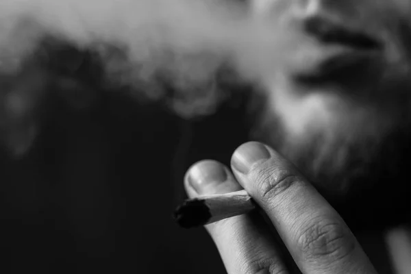 Un joint à la main Un homme fume de l'herbe de cannabis,. Fumée sur fond noir. Concepts de la consommation de marijuana médicale et de la légalisation du cannabis.Noir et blanc — Photo