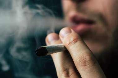 Esrar ot, onun ellerini A adam ortak bir çekiyor. Siyah bir arka plan üzerinde duman. Tıbbi esrar kullanım ve yasallaştırma esrar kavramları.