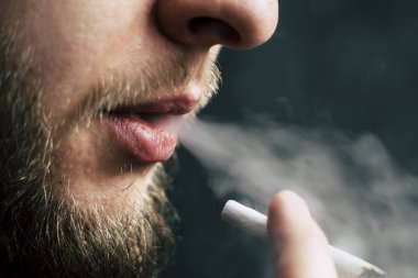 Bir adam sigara esrar esrar, esrar ve çakmak elinde. Siyah bir arka plan üzerinde duman. Tıbbi esrar kullanım ve yasallaştırma esrar kavramları.