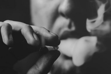 Esrar ot, onun ellerini A adam ortak bir çekiyor. Siyah bir arka plan üzerinde duman. Tıbbi esrar kullanım ve yasallaştırma esrar kavramları. Siyah ve beyaz