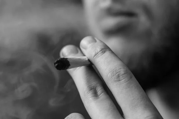 一个男人抽大麻, 手里拿着打火机。黑色背景下的烟雾。医疗用大麻的概念和大麻的合法化。黑白相间 — 图库照片