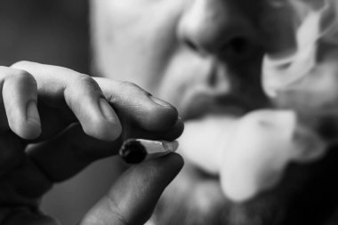 Bir adam sigara esrar esrar, esrar ve çakmak elinde. Siyah bir arka plan üzerinde duman. Tıbbi esrar kullanım ve yasallaştırma esrar kavramları. Siyah ve beyaz