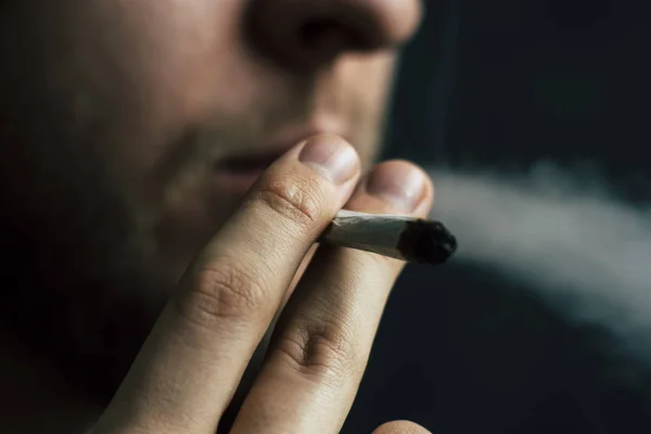 Fuma marihuana, un porro y un encendedor en sus manos. Humo sobre fondo negro. Conceptos de uso médico de la marihuana y legalización del cannabis . — Foto de Stock