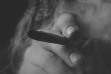 Bir adam ot Esrar sigara esrar ve çakmak onun ellerinde. Siyah bir arka plan üzerinde duman. Tıbbi esrar kullanım ve yasallaştırma esrar kavramları. Siyah ve beyaz