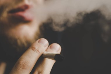 Bir adam sigara esrar esrar, esrar ve çakmak elinde. Siyah bir arka plan üzerinde duman. Tıbbi esrar kullanım ve yasallaştırma esrar kavramları.