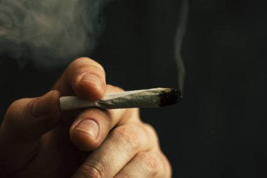adam elinde ortak. Bir adam esrar ot çekiyor bir. Siyah bir arka plan üzerinde duman. Tıbbi esrar kullanım ve yasallaştırma esrar kavramları.