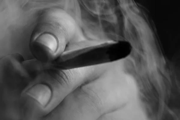 Ένας άνθρωπος καπνίζει κάνναβη ζιζάνιο μια κοινή και ένα ελαφρύτερο στα χέρια του. Καπνού σε μαύρο φόντο. Έννοιες της ιατρική χρήση μαριχουάνα και τη νομιμοποίηση της κάνναβης. Μαύρο και άσπρο — Φωτογραφία Αρχείου