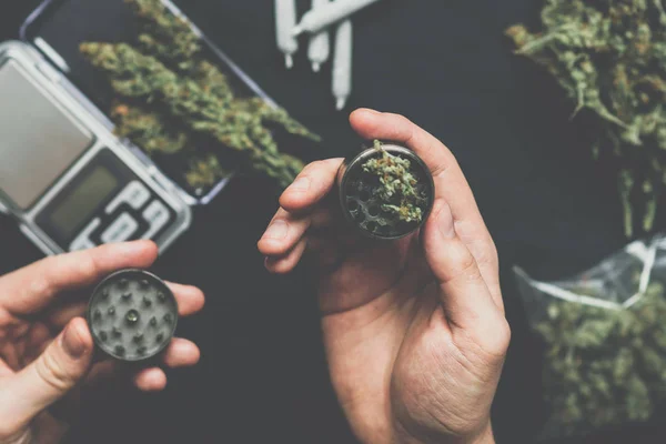Een man een grinder gebruikt om te slijpen marihuana onkruid tegen een toppen cannabis vintage kleur — Stockfoto