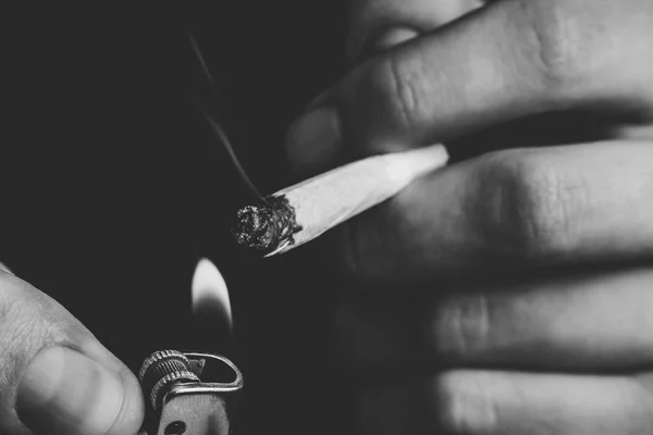 Articulación en mano. Un hombre fuma marihuana, una. Humo sobre fondo negro. Conceptos de uso medicinal de la marihuana y legalización del cannabis.Blanco y negro — Foto de Stock