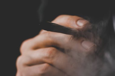 Esrar otu A adam sigara, bir ortak ve bir çakmak onun elinde. Siyah bir arka plan üzerinde duman. Tıbbi esrar kullanım ve yasallaştırma esrar kavramları.
