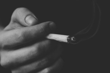 adam elinde ortak. Bir adam esrar ot çekiyor bir. Siyah bir arka plan üzerinde duman. Tıbbi esrar kullanım ve yasallaştırma esrar kavramları. Siyah ve beyaz