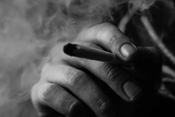 Fumée sur fond noir. Un homme fume de l'herbe de cannabis, un joint et un briquet dans ses mains. Concepts de la consommation de marijuana médicale et de la légalisation du cannabis.Noir et blanc — Photo