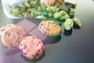 Çikolata ve üzerinde esrar ve tomurcuk tomurcukları olan kurabiyeler. Kurabiye ve CBD otlu çikolata kavramı. Gıda ve siyah arkaplanda tıbbi marihuana kullanımı.