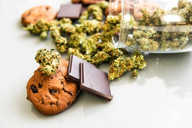 Esrarlı kurabiyeler ve masada esrar tomurcukları. Kenevir otlu kurabiyeler CBD. Gıda ve beyaz arka planda kullanılmak üzere tıbbi marihuana tedavisi.