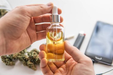 Elinde pipette bir şişe yağ keneviri, beyaz arka planda CBD kenevir yağı, tıbbi marihuana konsepti, kapanış, kenevir ürünü,