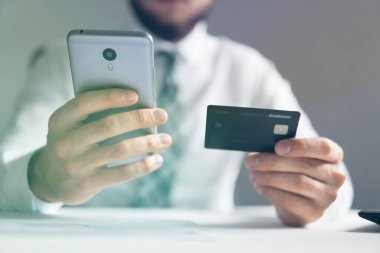 Çevrimiçi ödemeler telefonla. Çevrimiçi döviz ticareti. Elinde banka kartı olan genç bir iş adamı. Akıllı telefon ve internet ticareti. Malların çevrimiçi ödemesi.