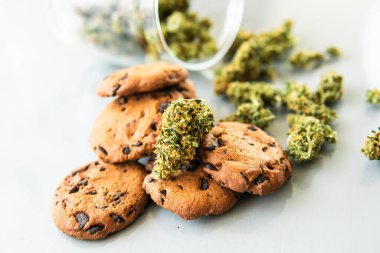 Esrarlı kurabiyeler ve masada esrar tomurcukları. Kenevir otlu kurabiyeler CBD. Gıda ve beyaz arka planda kullanılmak üzere tıbbi marihuana tedavisi.