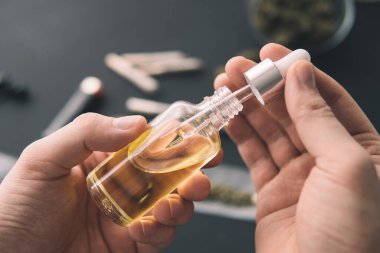 Tıbbi marihuana konsepti, yakın çekim, kenevir ürünü, CBD kenevir yağı. El ele tutuşan kenevir yağı şişesi pipette, doğal otlar.,