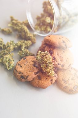 Esrarlı kurabiyeler ve masada esrar tomurcukları. Gıda ve beyaz arka planda tıbbi marihuana kullanımı. Kenevir otlu kurabiyeler CBD. Dikey çekim