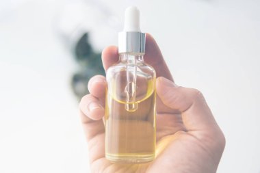 Elinde pipette bir şişe kenevir yağı, tıbbi marihuana konsepti, yakın plan, CBD kenevir yağı. kenevir ürünü, ışık renk tonları sızdırıyor