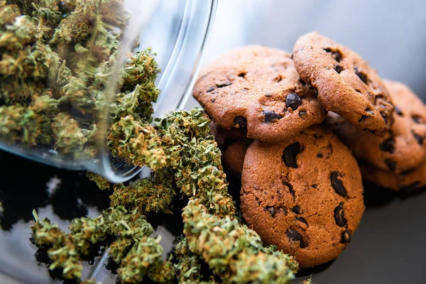 Treatment of medical marijuana for use in food, black background. Concept of cooking with cannabis herb. Cookies with cannabis and buds of marijuana on the table.