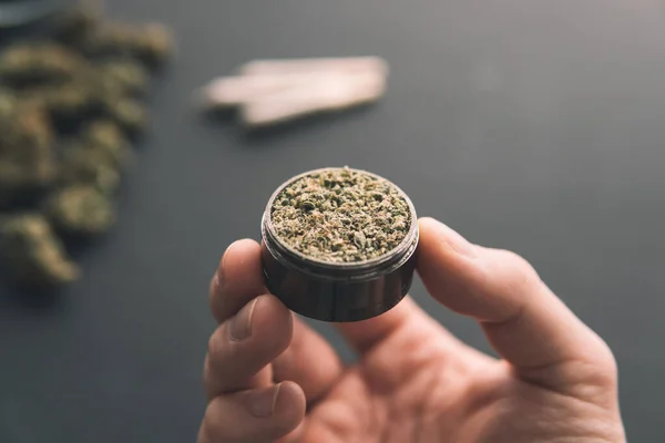 in hand grinder with fresh marijuana , Cannabis buds on black table, joint with weed, top view close up,