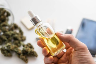 Beyaz arka planda CBD kenevir esrarı, elinde bir şişe petrol keneviri, kenevir ürünü, tıbbi marihuana konsepti, kapat,