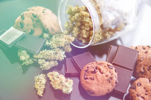 Treatment of medical marijuana for use in food, black background. Concept of Cookies and chocolate with cannabis herb CBD. Chocolate and Cookies with cannabis and buds of marijuana on the table.