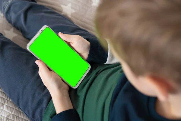 Smartphone with a green screen in hand child . close up top view Phone a for keying is holding kid. Smartphone with a hromakey in the hands of a child.