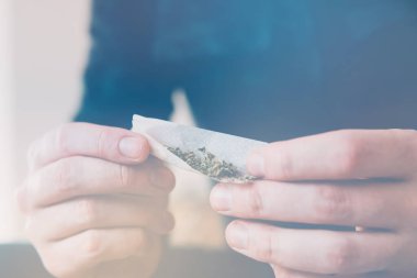Uyuşturucu narkotik konsepti. Esrar saran bir adam. Marihuana hazırlayan ve yuvarlayan adam. Uyuşturucu kullanımı. Kapatın. Marihuanayı çakmakla yakan bağımlıya yakın..