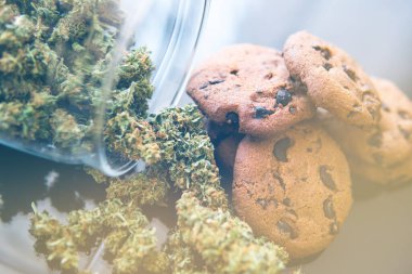 Yiyecek ve siyah arka planda tıbbi marihuana kullanımı. Kenevir bitkisi CBD ile yemek pişirme kavramı. Esrarlı kurabiyeler ve masada esrar tomurcukları. ışık sızıntısı