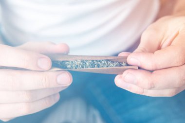 Marihuana hazırlayan ve yuvarlayan bir adam. Marihuana öğütücü esrar kullanımı kavramı. Beyaz arkaplanda esrar saran bir adamı kapat.