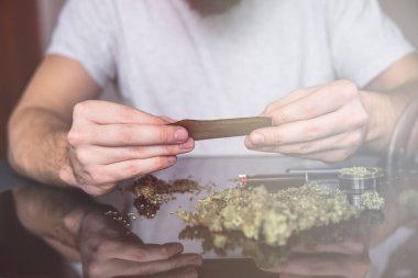 Esrarkeşin çakmakla esrar içtiği yeri kapatın. Esrar saran bir adam. Uyuşturucu kullanımı. Kapatın. Uyuşturucu narkotik konsepti. Marihuana hazırlayan ve yuvarlayan adam.