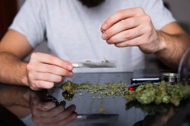 Uyuşturucu narkotik konsepti. Esrar saran bir adam. Uyuşturucu kullanımı. Kapatın. Marihuana hazırlayan ve yuvarlayan adam. Marihuanayı çakmakla yakan bağımlıya yakın..