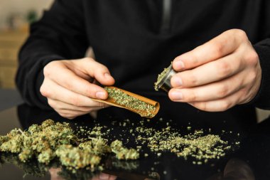 Esrarkeşin çakmakla esrar içtiği yeri kapatın. Esrar saran bir adam. Marihuana hazırlayan ve yuvarlayan adam.