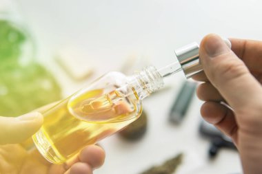 Eldeki pipette bir şişe yağ keneviri, yakın çekim, kenevir ürünü, beyaz arka planda CBD kenevir yağı, tıbbi marihuana konsepti, ışık sızdıran renk tonları