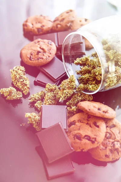 Treatment of medical marijuana for use in food, black background. Chocolate and Cookies with cannabis and buds of marijuana on the table. Cookies and chocolate with cannabis Vertical shot