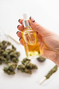 Yakın plan, tıbbi kenevir konsepti, pipette kadın elinin yağlı kenevir CBD 'si, beyaz arka planda marihuana özü, ot ürünü, dikey çekim