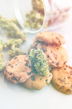 Esrarlı kurabiyeler ve masada esrar tomurcukları. Kenevir otlu kurabiyeler CBD. Gıda ve beyaz arka planda tıbbi marihuana kullanımı. Dikey çekim ışığı sızıntısı