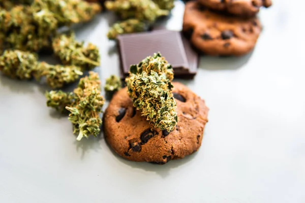 Treatment of medical marijuana for use in food, white background. Cookies with cannabis herb CBD. Cookies with cannabis and buds of marijuana on the table.